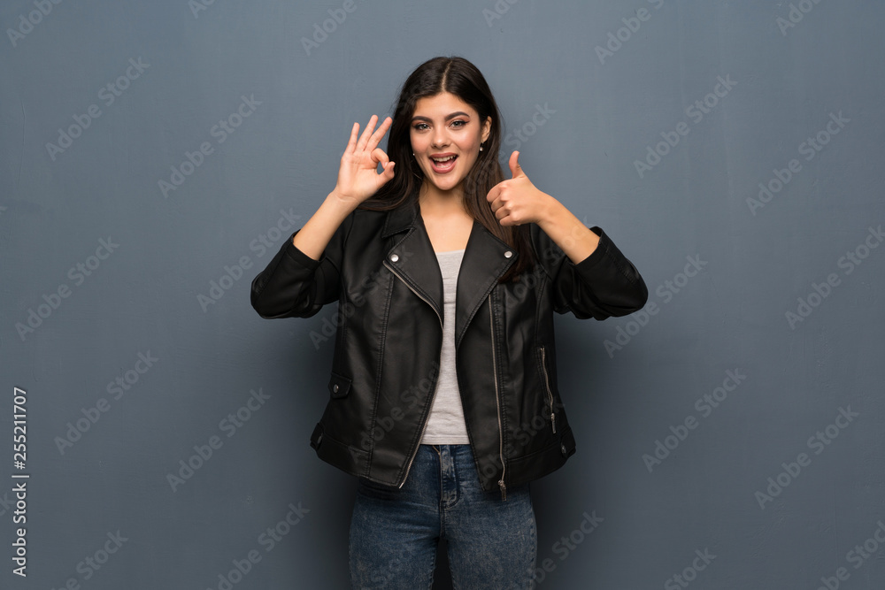 Teenager girl over grey wall showing ok sign with and giving a thumb up gesture