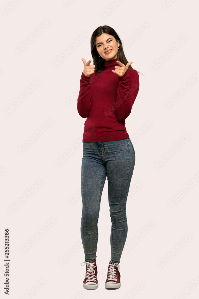A full-length shot of a Teenager girl with turtleneck pointing to the front and smiling over isolated background A full-length shot of a Teenager girl with turtleneck pointing to the front and smiling over isolated background