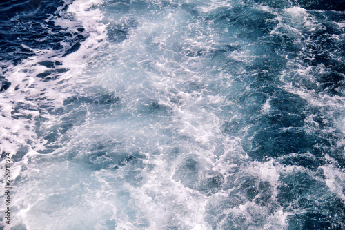 Turbulence made by foam of sea water from a high-speed yacht on surface of sea. Blue sea waves with lot of sea foam. Surface of sea with waves, splash, foam and bubbles, blue background and wallpaper.