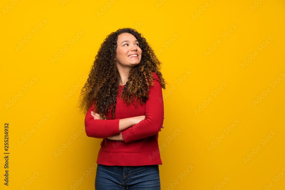 Teenager girl with red sweater over yellow wall looking up while smiling Teenager girl with red sweater over yellow wall looking up while smiling