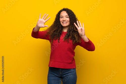 Teenager girl with red sweater over yellow wall counting nine with fingers