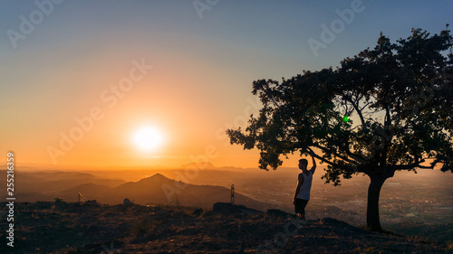 Chico agarrado a un   rbol viendo un atardecer en la monta  a