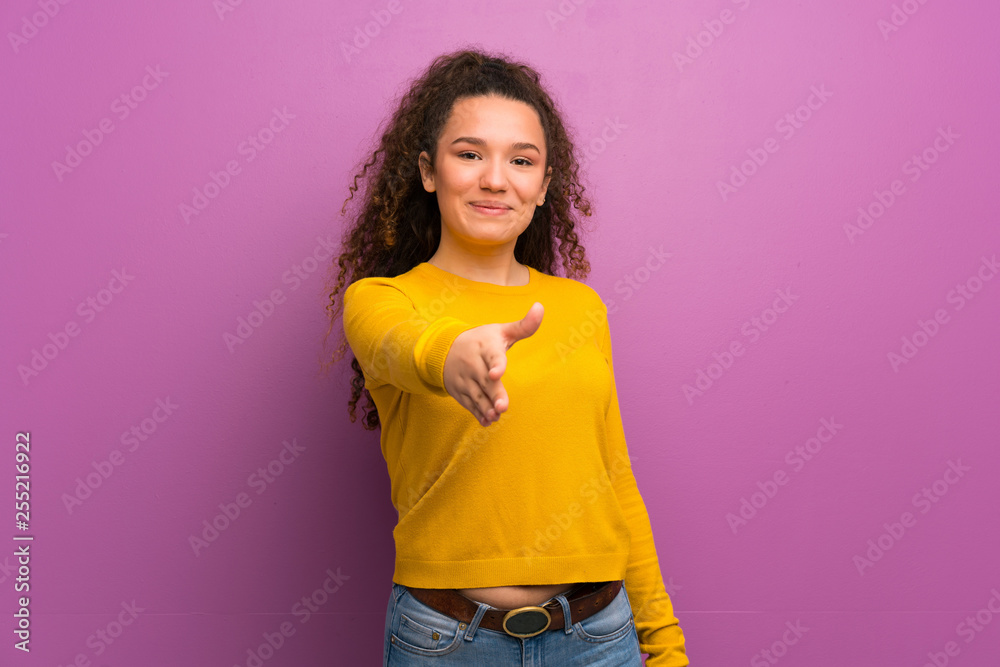 Teenager girl over purple wall shaking hands for closing a good deal Teenager girl over purple wall shaking hands for closing a good deal
