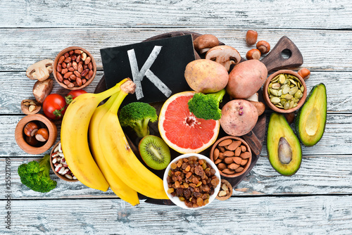 Foods containing natural potassium. K: Potatoes, mushrooms, banana, tomatoes, nuts, beans, broccoli, avocados. Top view. On a white wooden background. photo
