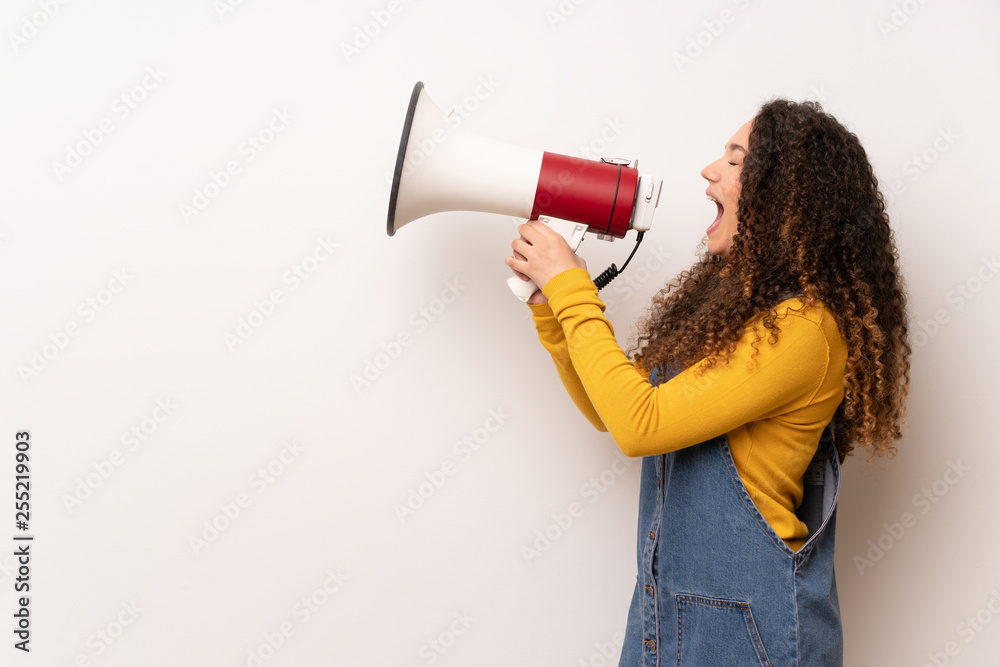 Teenager girl with red sweater over white wall shouting through a megaphone Teenager girl with red sweater over white wall shouting through a megaphone