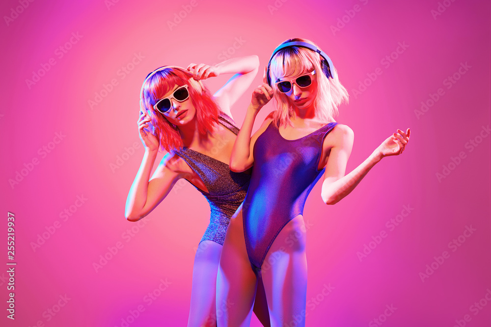 Fashion. Two DJ girl with Dyed Hair in Colorful neon light enjoy music,  friends. Party disco 80s 90s vibes. Model woman in fashionable bodysuit  dance, makeup. Creative art pink color Photos