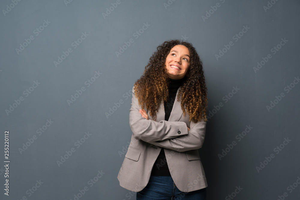 Teenager girl over blue wall looking up while smiling Teenager girl over blue wall looking up while smiling