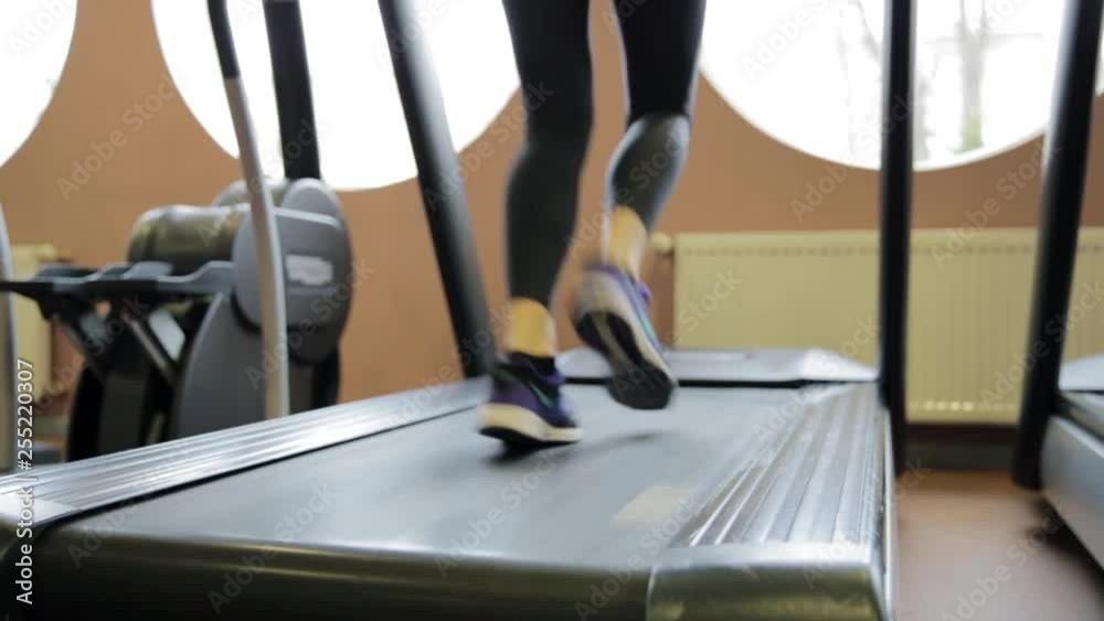 Fitness girl running on treadmill. Woman with muscular legs in gym