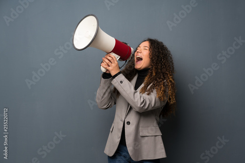 Teenager girl over blue wall shouting through a megaphone