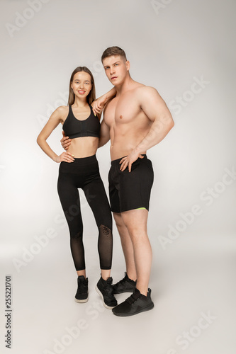 Shirtless athletic man and young woman in black sportswear posing over grey background