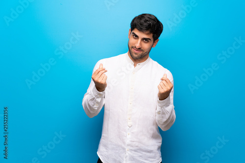 Young man over isolated blue wall making money gesture