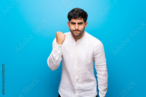 Young man over isolated blue wall with angry gesture