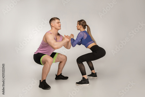 Young attractive couple in trendy sportswear doing sguats together