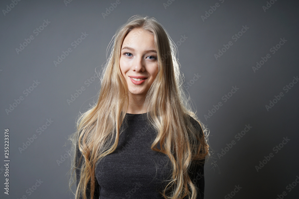 teen girl with long blond hair and radiant smile - studio portrait of young woman against gray background with copy space teen girl with long blond hair and radiant smile - studio portrait of young woman against gray background with copy space
