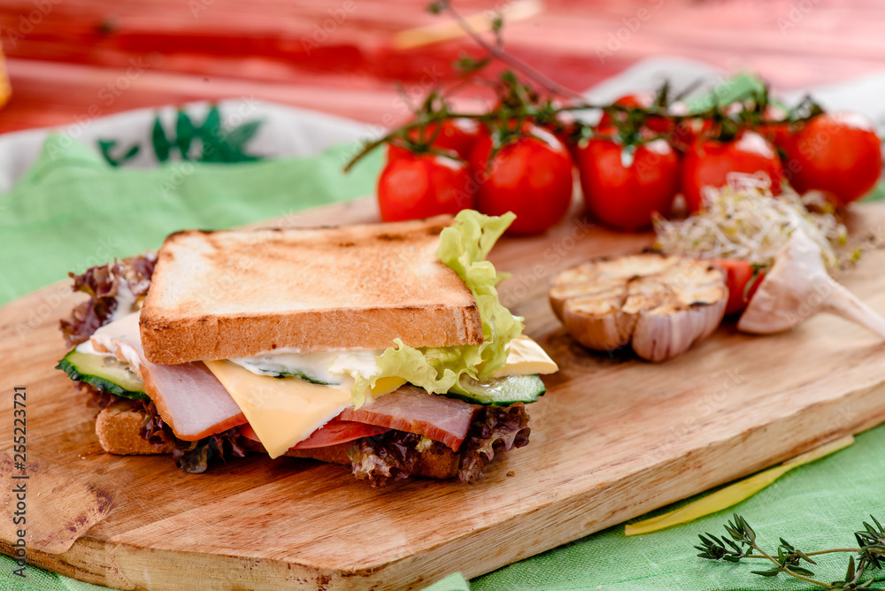Sandwich with ham, tomatoes, cheese, sauce and lettuce on a wooden board and napkins among vegetables. close up Sandwich with ham, tomatoes, cheese, sauce and lettuce on a wooden board and napkins among vegetables. close up
