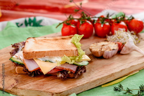 Sandwich with ham, tomatoes, cheese, sauce and lettuce on a wooden board and napkins among vegetables. close up