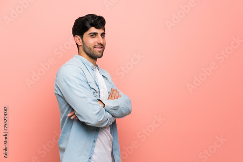 Young man over pink wall with arms crossed and looking forward © luismolinero