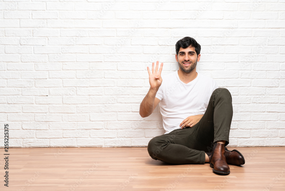Young man sitting on the floor happy and counting four with fingers Young man sitting on the floor happy and counting four with fingers