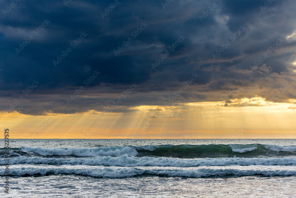 Obraz premium colorful sunset with wave in the forreground at Piha Beach, New Zealand