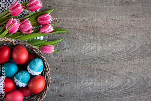  Wielkanocne tło z różowo-białymi tulipanami i koszykiem pełnym kolorowych pisanek ozdobionych koronką photo