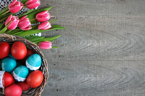 Wielkanocne tło z różowo-białymi tulipanami i kolorowymi pisankami w koszyku