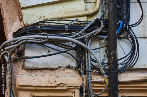 Wires - electrical, telephone, antenna, computer, network on the wall of a dilapidated house with peeling plaster, separate wires in metal pipes with protection