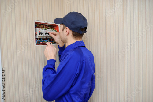 lateral view of a young eletrician in blue overall disassembling a electrical panel with fuses in a house. photo