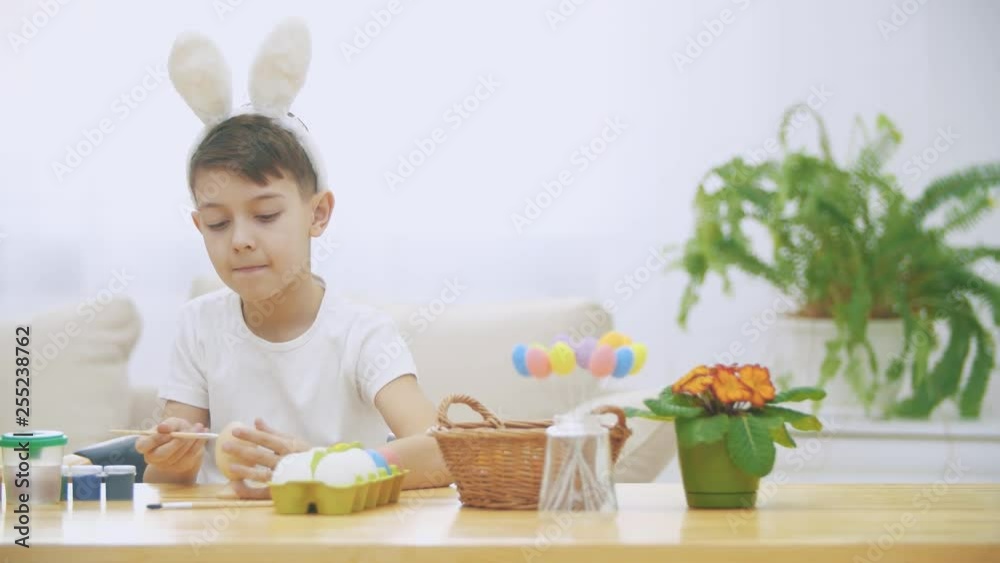 Little bunny-boy is trying to paint an Easter egg with a help of nude brush. Happy boy is smiling widely and sincerely Little bunny-boy is trying to paint an Easter egg with a help of nude brush. Happy boy is smiling widely and sincerely