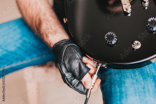 A man in black leather gloves connects a cable to an electric guitar - plug and play photo