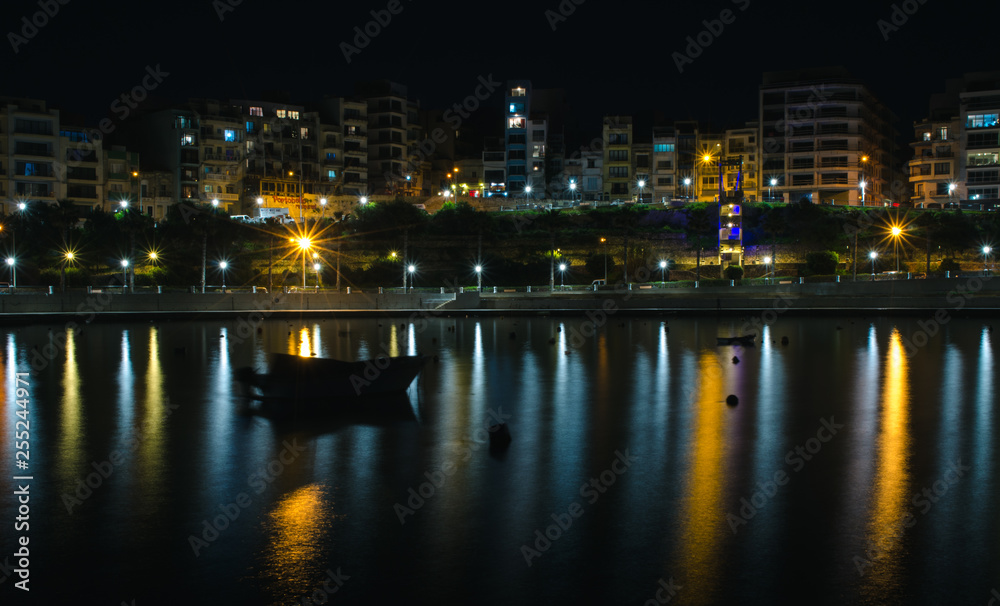 Beautiful night picture of Buġibba, St. Paul's Bay, a town in the Northern Region of Malta. Night lights of the city reflected in the sea.