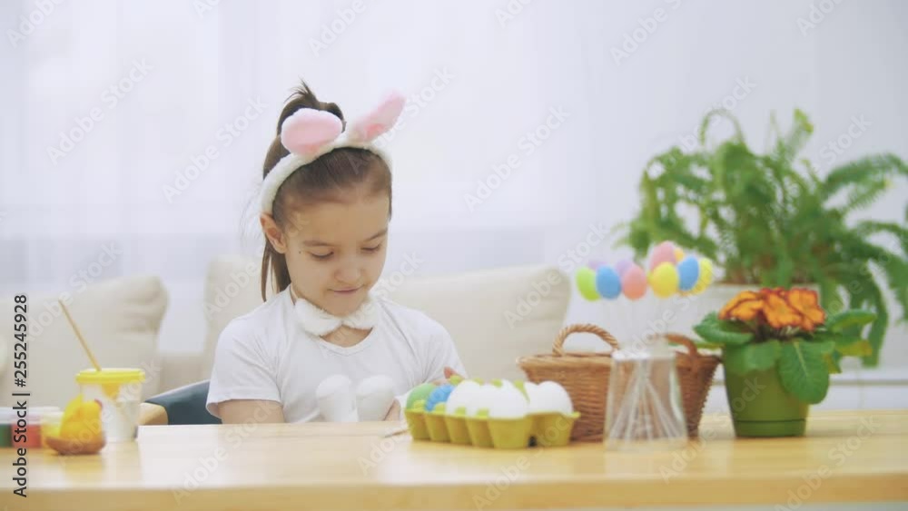 Nice, cute girl is having fun paiting with Easter bunny, Adorable girl is lulling bunny and cudding it. Girl with a beauty spot at her face and is smiling gently, sitting at the wooden table with Nice, cute girl is having fun paiting with Easter bunny, Adorable girl is lulling bunny and cudding it. Girl with a beauty spot at her face and is smiling gently, sitting at the wooden table with