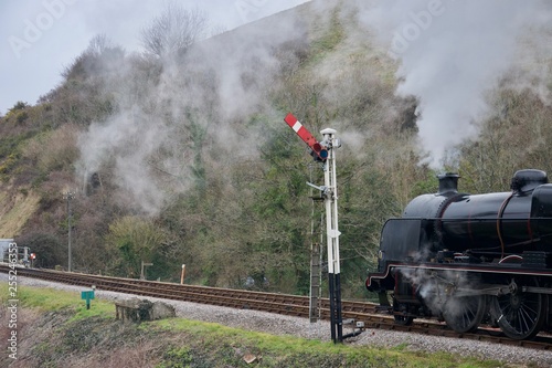 Black steam train on railway line (track) under hill near signal post