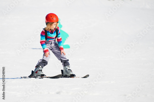 Child girl skiing in mountains. Active kid with safety helmet and goggles. Ski race for young children. Kids ski lesson in alpine school. Little skier racing in snow