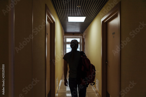 A young woman with a backpack is walking along the corridor of the hotel to her room. Silhouette of a girl with a backpack