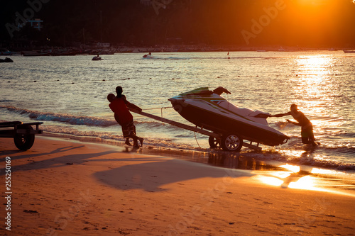 Wallpaper Mural Men at sunset pull hydrocycle out of the water on a sandy beach.  Summer vacation. Water bike loaded onto a trailer Torontodigital.ca