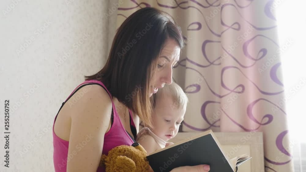 Happy mother reading a book to child boy indoors. Sweet moment with mother reading book to baby.