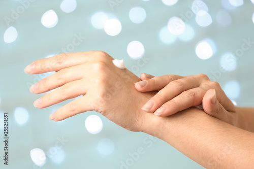 Woman applying hand cream on blurred background, closeup