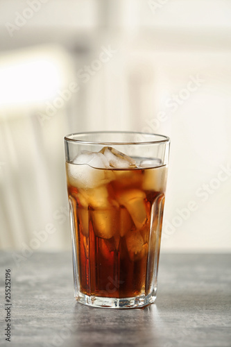 Glass of cola with ice on table against blurred background, space for text