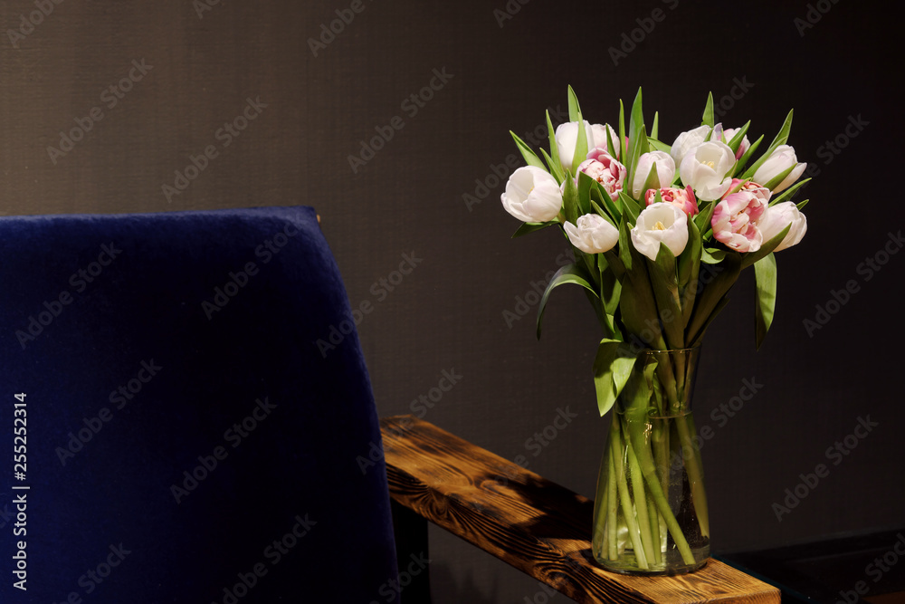 A bouquet of tulips of different colors, white, pink, stands in a glass vase in a dark interior. A bouquet of tulips of different colors, white, pink, stands in a glass vase in a dark interior.