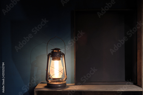 Vintage antique kerosene lamp against a dark blue wall. Wooden shelves.