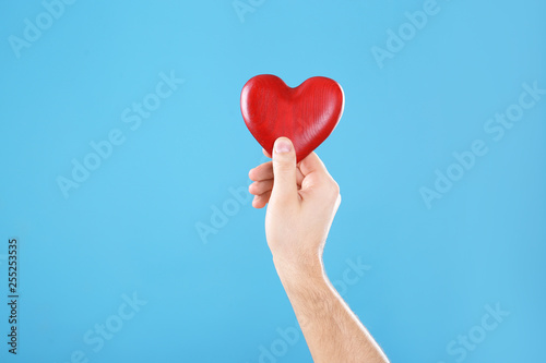 Man holding decorative heart in hand on color background