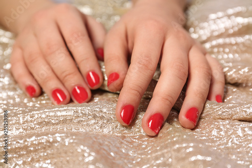 Woman with red manicure on gold fabric, closeup. Nail polish trends