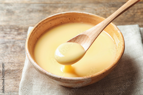 Spoon with pouring condensed milk over bowl on table, closeup. Dairy products