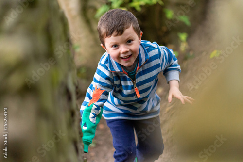 A small boy in bright clothes climbs through a forest whilst smiling