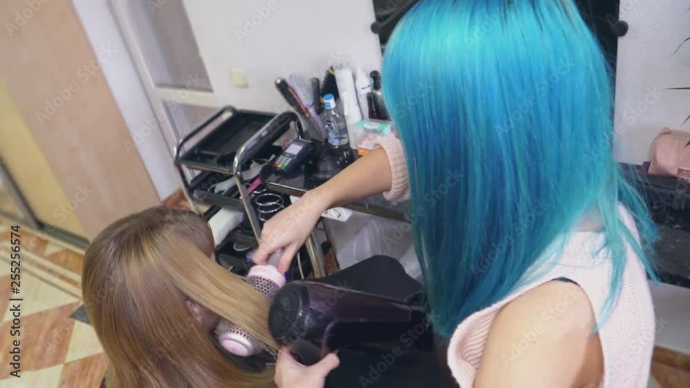 A hairdresser with blue hair dries and combs girl hair A hairdresser with blue hair dries and combs girl hair