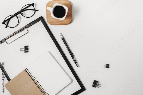 Flat lay, top view office table desk. Workspace with blank clip board, watch, office supplies, pen, eyeglasses and coffee cup on white background. Copy space