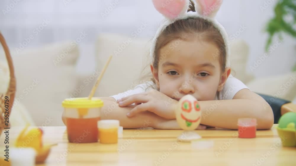 Tired sleepy cute girl is lying down the table and watching at her creation. Colourised funny Easter egg. Tired sleepy cute girl is lying down the table and watching at her creation. Colourised funny Easter egg.