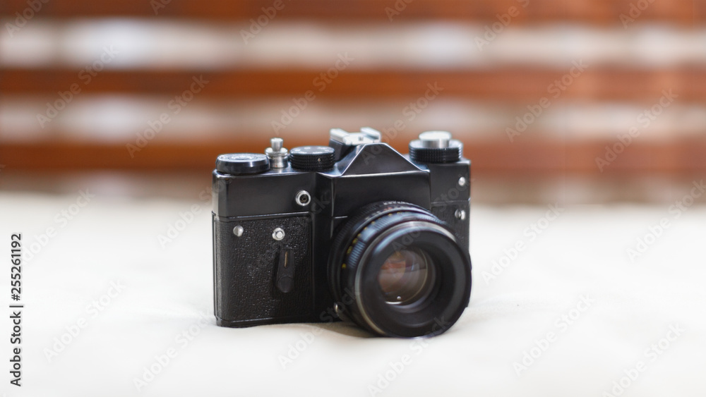 Close up photo of black soviet vintage camera lying on the light surface, front view/ analog retro film photo camera, manual lens, selective focus on SLR/ art concept.