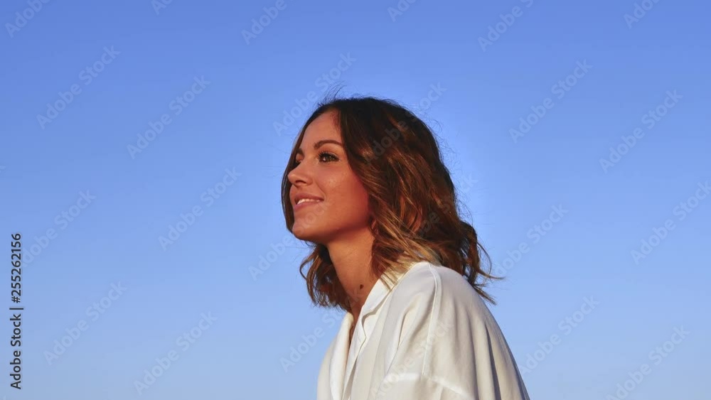Pensive young woman face looking away at dawn outdoors. Close up profile portrait of beautiful girl with long wavy hair lonely, hopeful, thinking On blue sky background Pensive young woman face looking away at dawn outdoors. Close up profile portrait of beautiful girl with long wavy hair lonely, hopeful, thinking On blue sky background