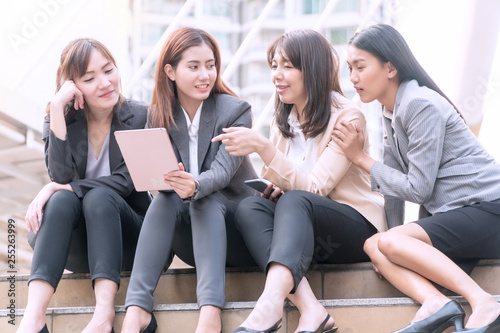 Group of businesswoman sitting in the shade on the stairs,looking at digital tablet in a modern city. Beautiful young woman wearing the business suit using tablet and laughing happily.